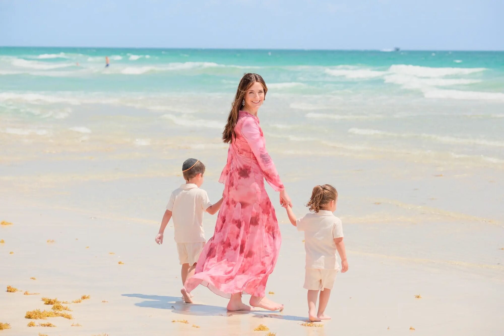 Miami Family Photographer | Mother & Children Session at South Beach A mother in a pink floral dress walking hand-in-hand with her two young sons along the shoreline at South Beach, Miami — captured by a Dreamgraphy Miami family photographer