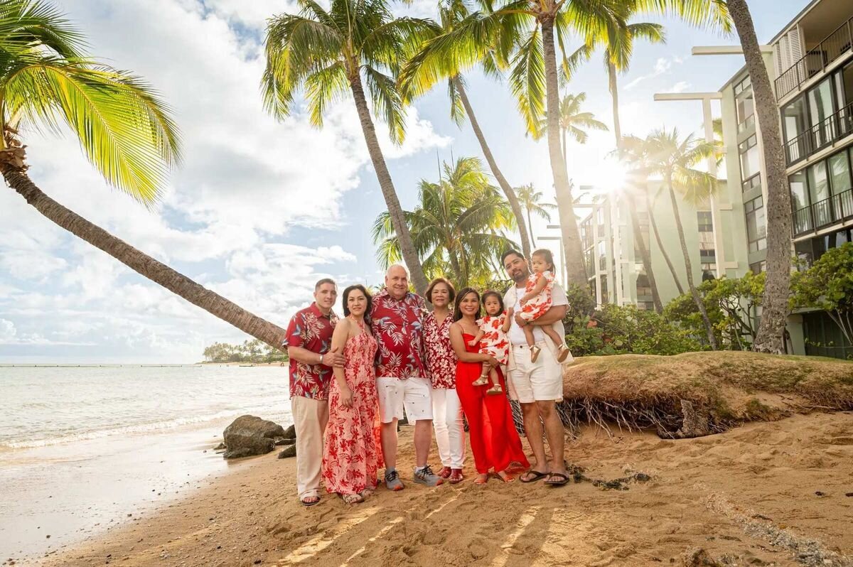 Multi-generational extended family in coordinating red and floral outfits posing on the beach under palm trees at Waialae beach, Oahu — family photos by Dreamgraphy