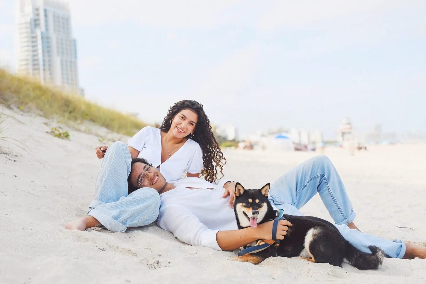 Couple relaxing on the sand with their dog during a candid engagement photo session at South Beach Miami