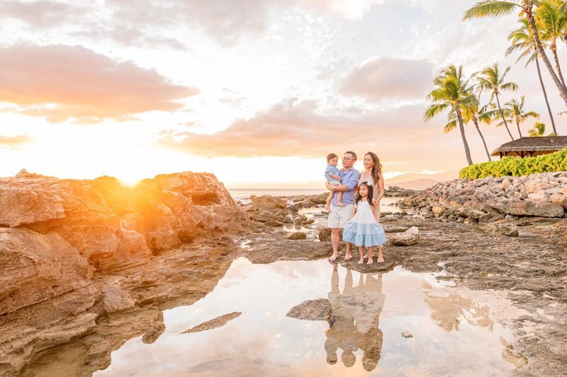 Family of four with lava rocks and palm trees in the background taking photos in Oahu, Hawaii during sunset time. 