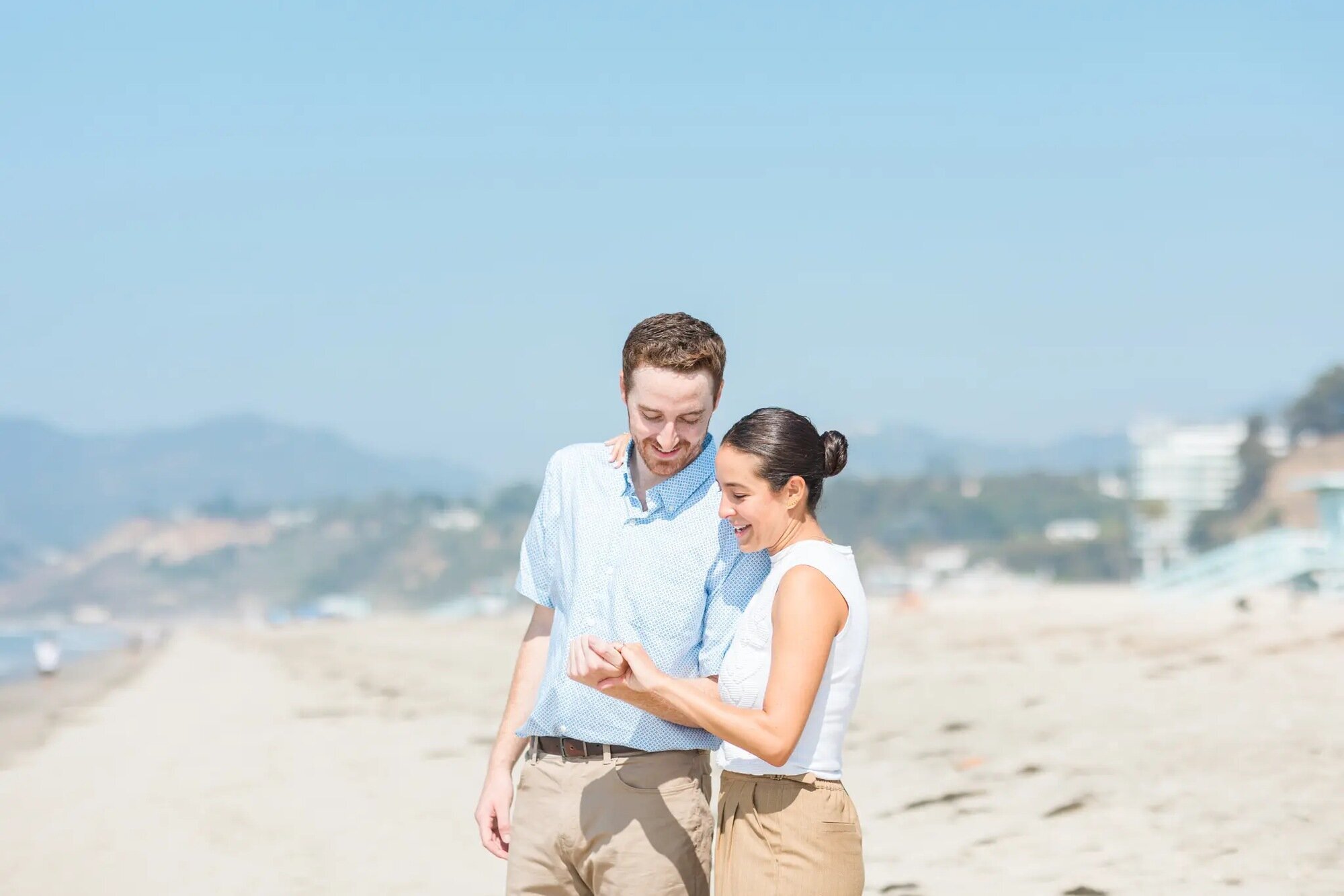Los Angeles Couples Photographer — Couples Session at Santa Monica Beach Los Angeles couples photographer capturing a couple walking hand in hand along Santa Monica Beach, smiling and looking at each other with the ocean and cliffs in the background