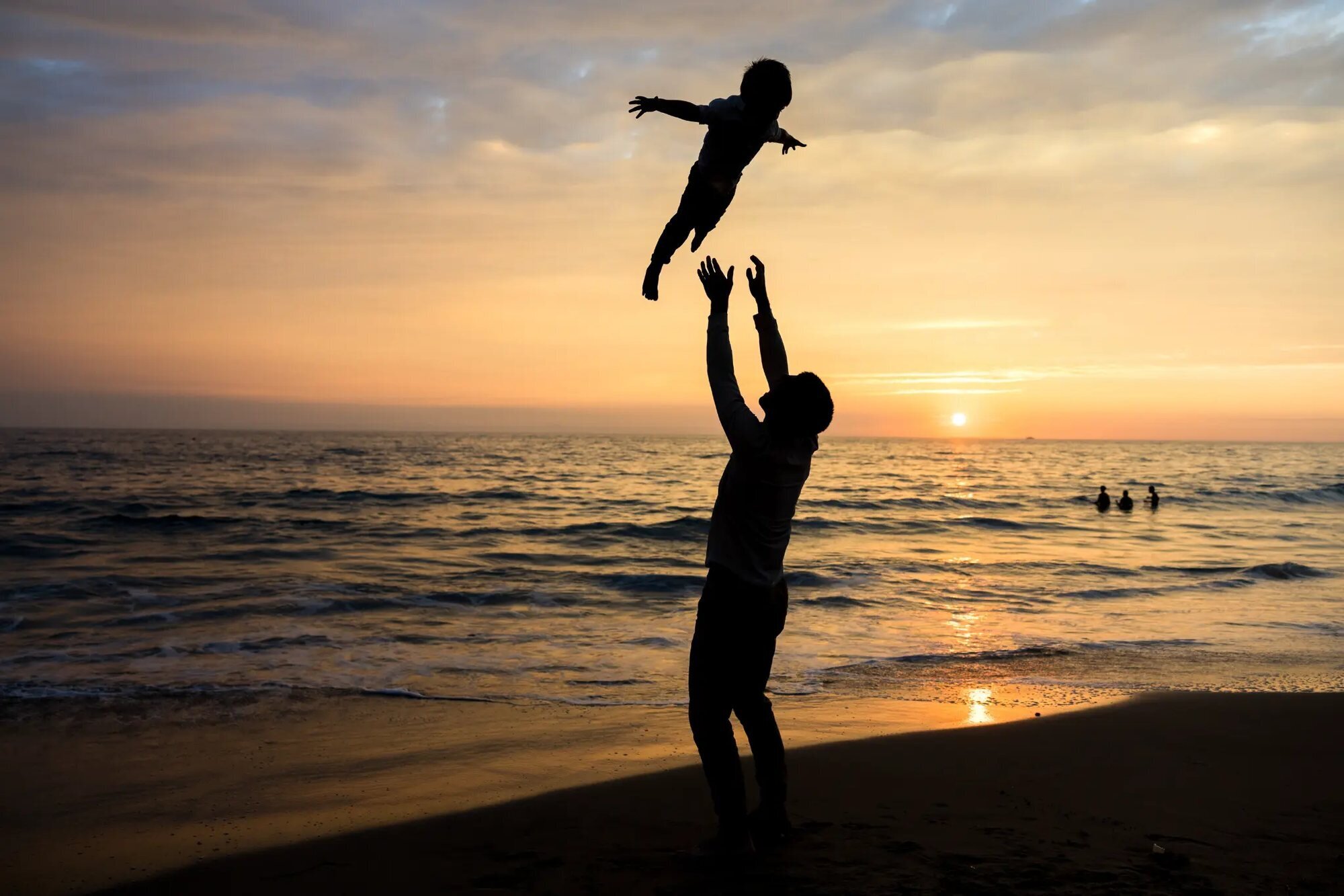 Los Angeles Family Photographer — Family Session at Santa Monica Beach at Sunset Los Angeles family photographer capturing a father tossing his young child high into the air on Santa Monica Beach at sunset, with the ocean and golden sky silhouetted behind them