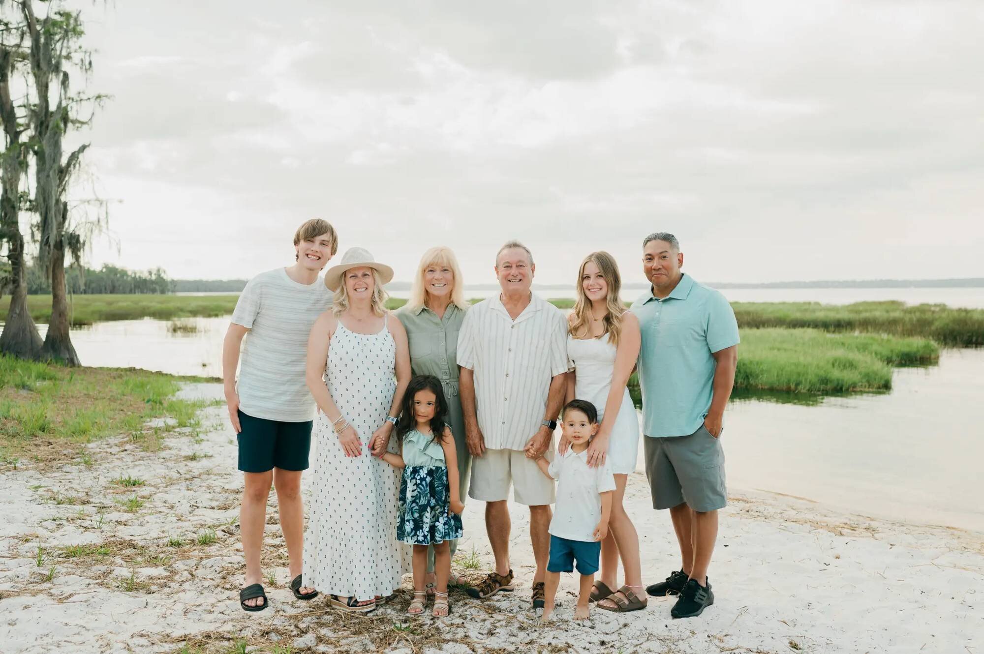 Extended family at Florida lakeside Multigenerational family of eight smiling together by a Florida lakeside with cypress trees and marshland behind them