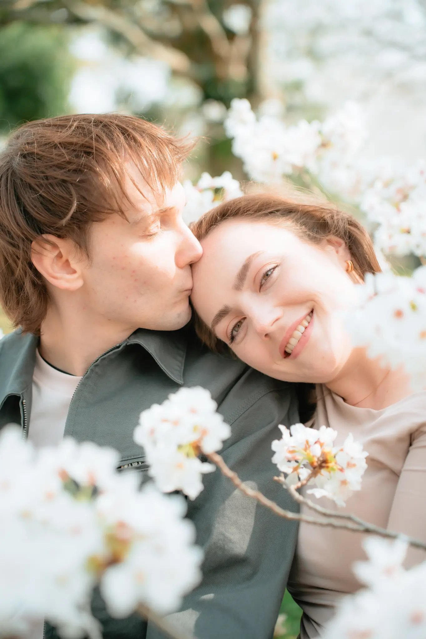 fukuoka-photographer-location-maizuru-park A man kisses a smiling woman on the forehead, framed by white blossoms in soft focus, at Maizuru Park in Fukuoka.