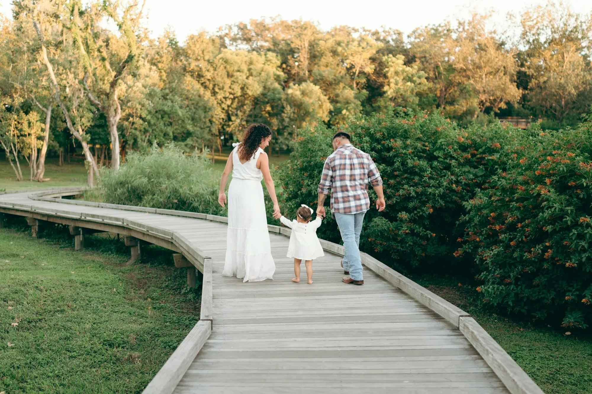 Family walking on wooden boardwalk Family of three walking hand in hand along a winding wooden boardwalk through a lush Florida park at golden hour