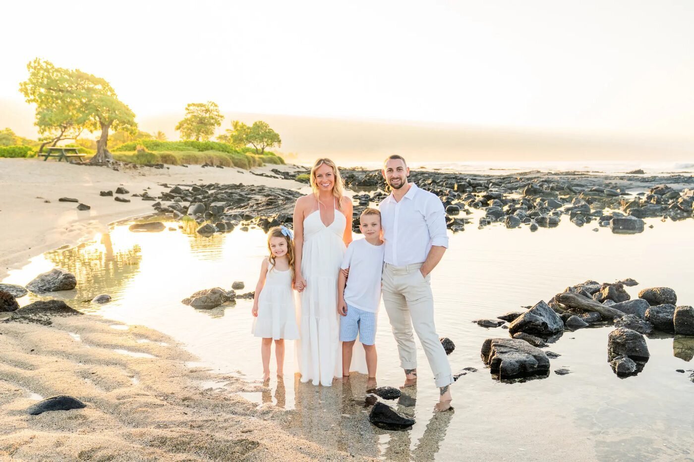 Big Island Family Photographer — Kohala Coast Golden Hour Session A family of four posing together on a Big Island beach during golden hour with lava rocks and warm sunset light behind them