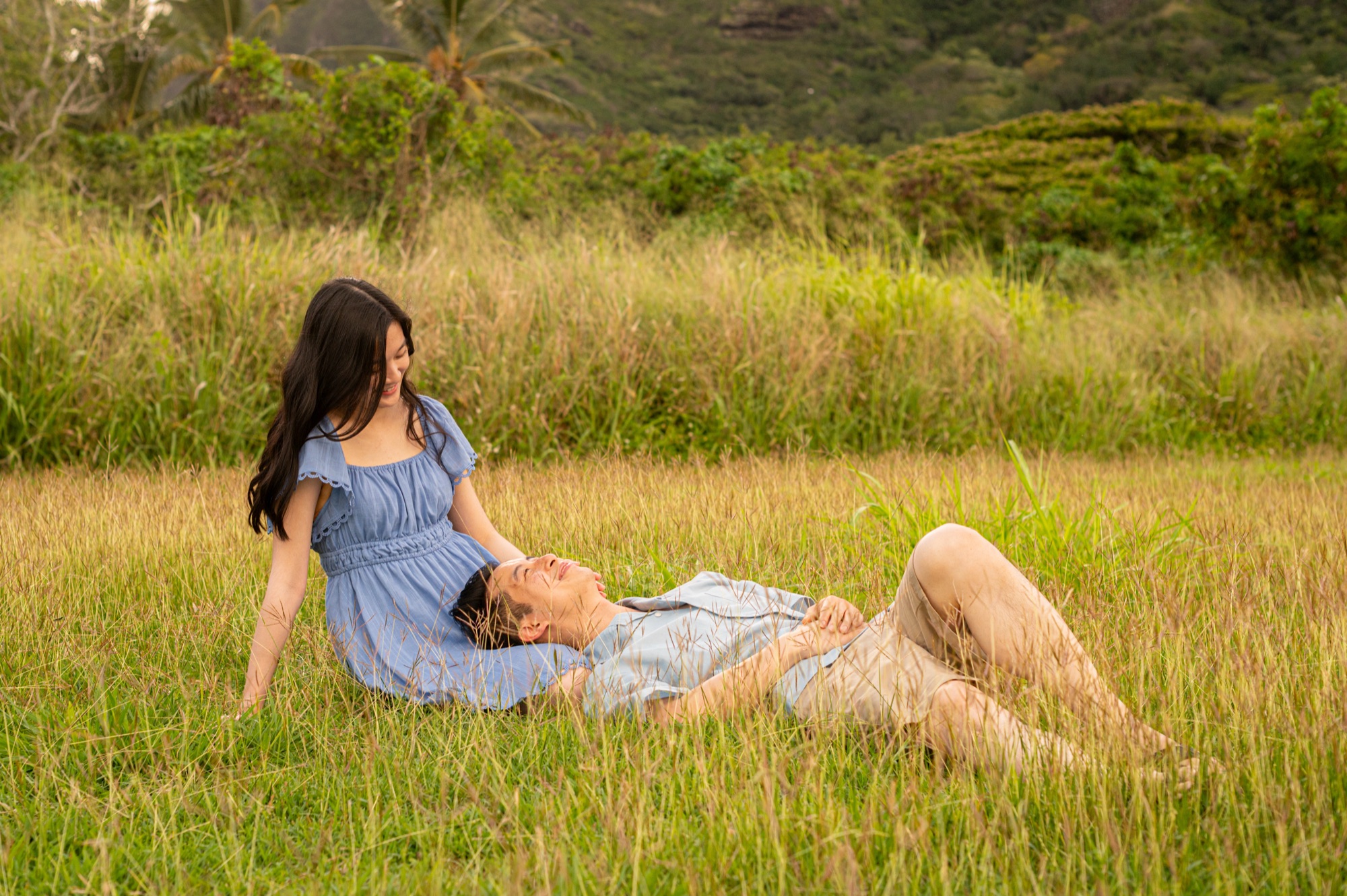 A couple relaxing in a grassy meadow, photographed from a distance, the man lying with his head in the woman's lap