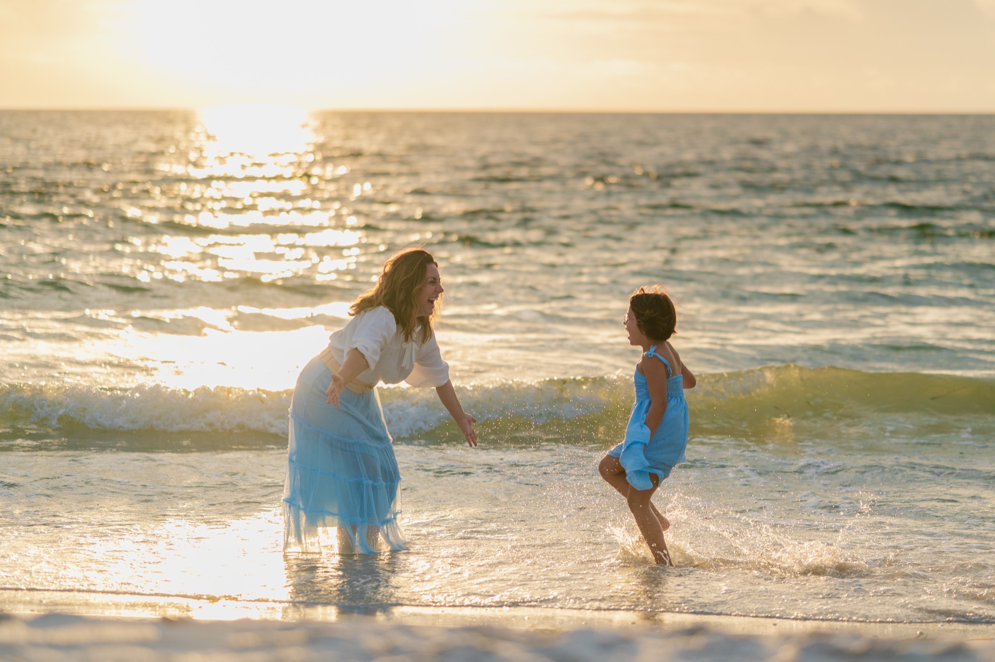 A mother and her daughter splashing and chasing each other in the shallow waves at sunset on St. Pete Beach, Tampa