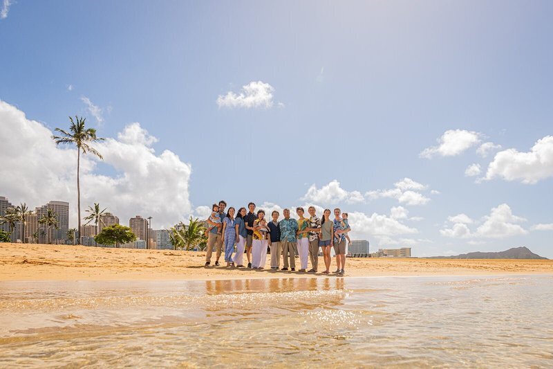 Large multi-generational extended family group portrait on the sand at Waikiki Beach, Oahu, with Diamond Head and the Honolulu skyline in the background — Oahu family photographer Dreamgraphy