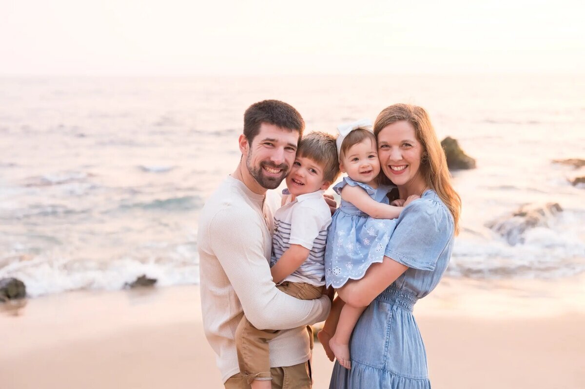 Los Angeles Photographer — Family Session at Crystal Cove State Beach Los Angeles photographer capturing a family of four smiling together on the sandy shores of Crystal Cove State Beach at sunset, with parents each holding a young child
