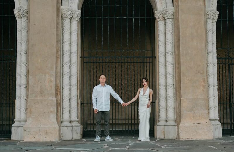 orlando-engagement-photographer-historic-arch-mobile A couple holding hands at arm's length in front of a carved stone archway with twisted columns and an iron gate in Orlando