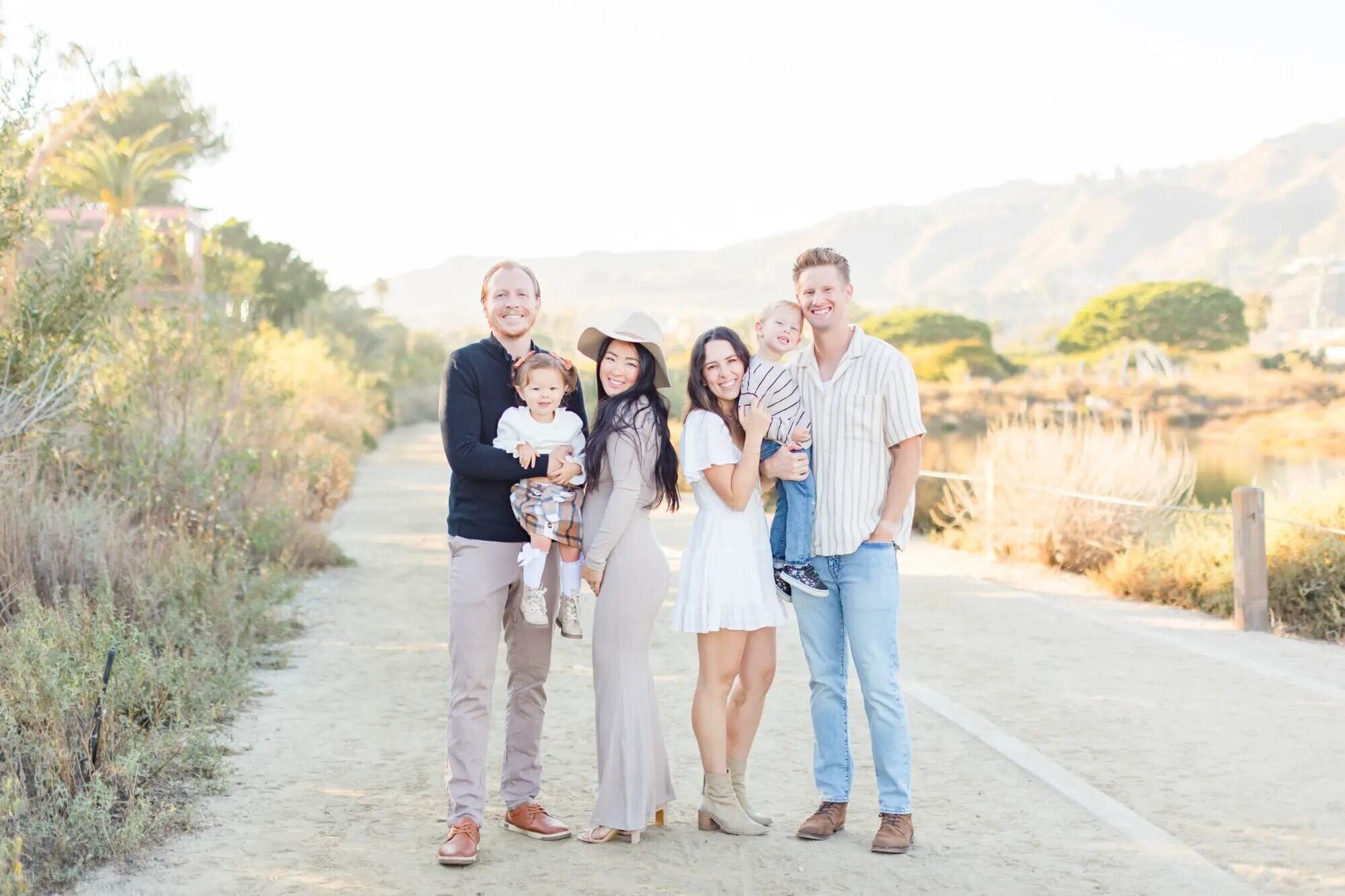 los-angeles-family-photographer-malibu-creek-state-park-session Two young families posing together on a sandy trail at Malibu Creek State Park during a golden hour session with a Los Angeles family photographer