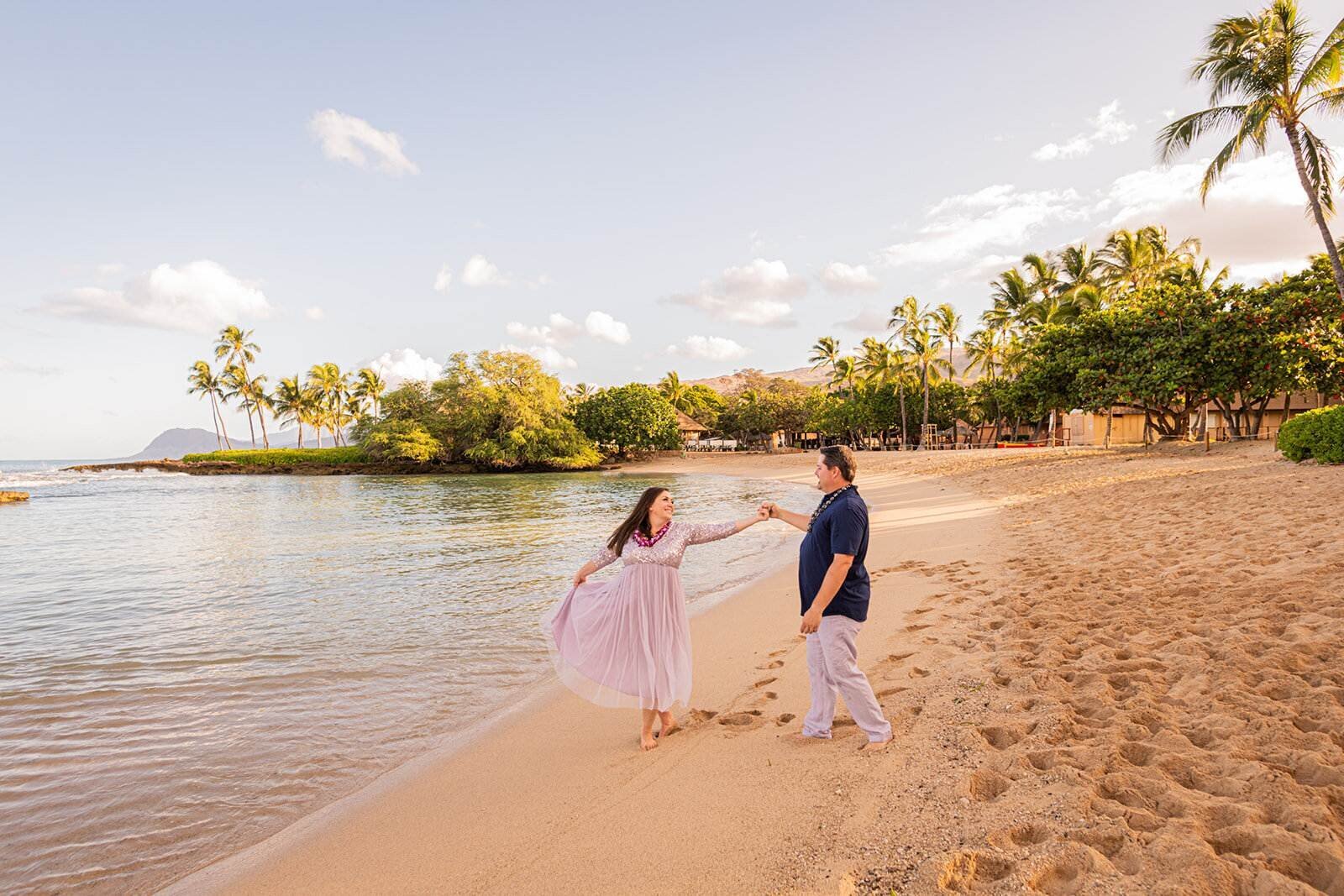Couple dancing and spinning on Ko Olina Beach at golden hour with calm water and palm trees behind them