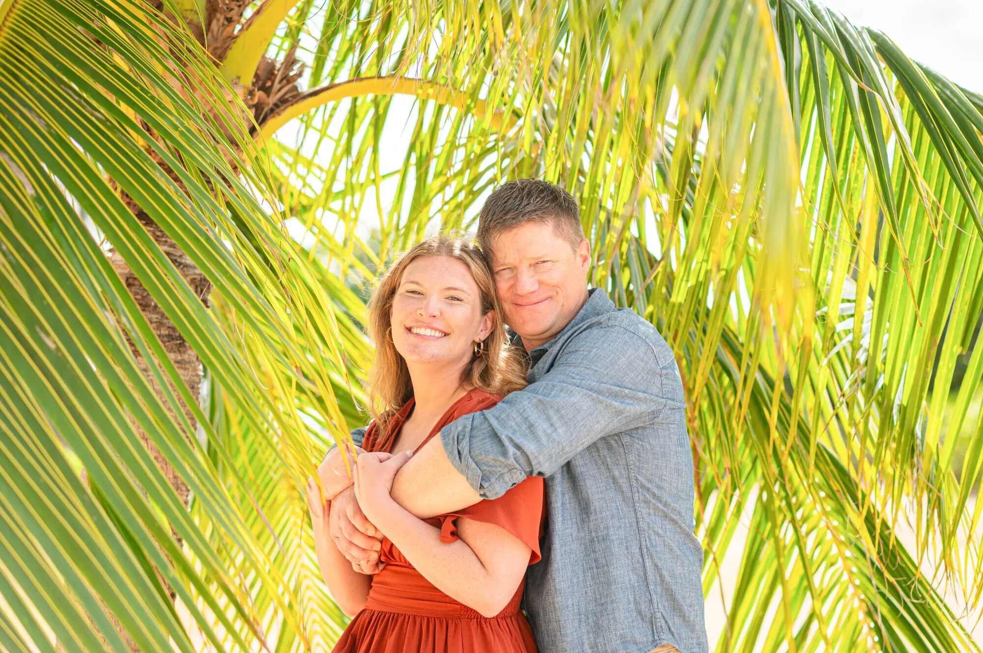 Couple smiling and embracing under palm fronds during an Oahu engagement photo session