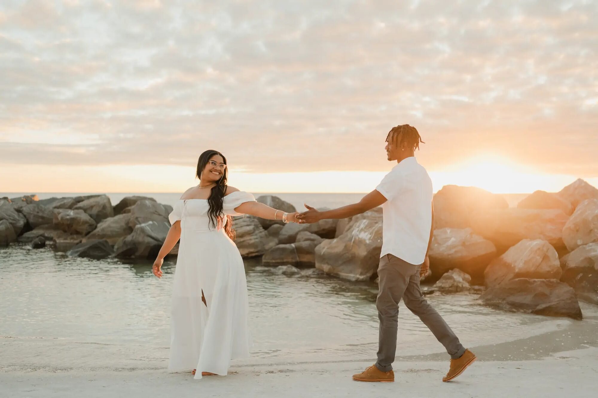 Couple Holding Hands at Beach Sunset — Vacation Photographer by Dreamgraphy A couple reaching for each other's hands on a sandy beach during a golden hour vacation photography session