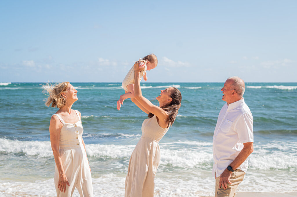  A joyful family with grandparents and a baby playing on a bright, sunny Hawaii beach, an example of a candid photo style that the photography quiz can help you plan for.