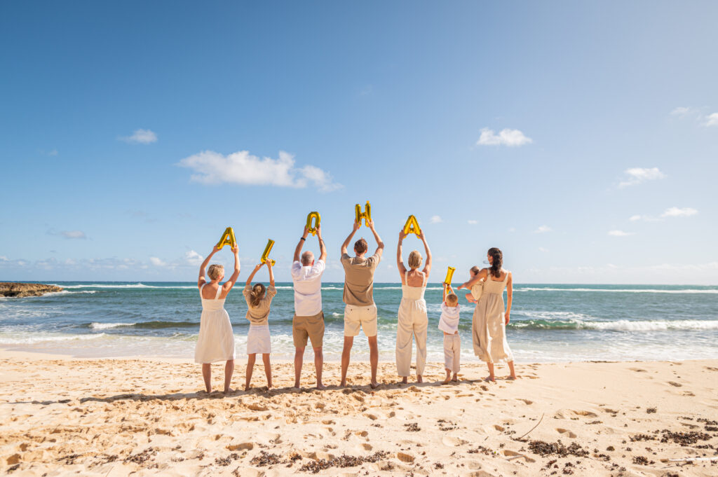  A family executing a creative photoshoot idea on a Hawaii beach, holding "ALOHA" balloons to show how the quiz helps choose the right timing—like bright sun vs. sunset—for a specific creative vision.
