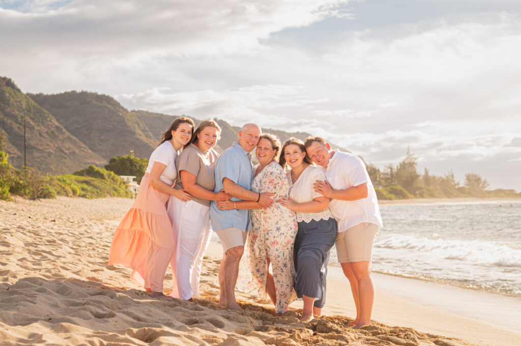 A large, multi-generational family hugging on a Hawaii beach during a golden hour sunset, the ideal result for clients who choose a "sunset session" in the family photography quiz.