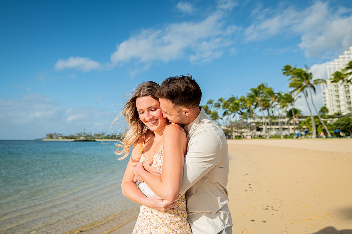 A couple embracing and smiling in front of lush tropical greenery after a beach proposal in Oahu, Hawaii — one of our favorite beach proposal ideas brought to life.